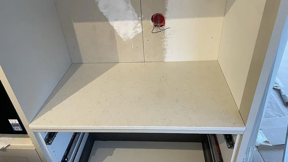 Kort bänkparti i polerad Silestone Snowy Ibiza med vit kompositsten och öppen köksstomme under montering i Gränna.