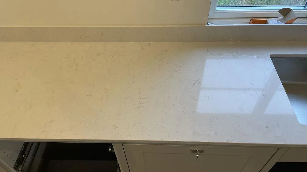 Polerad Silestone Snowy Ibiza-arbetsyta med ljus reflektion från fönstret och rostfri diskho i ett kök i Gränna.