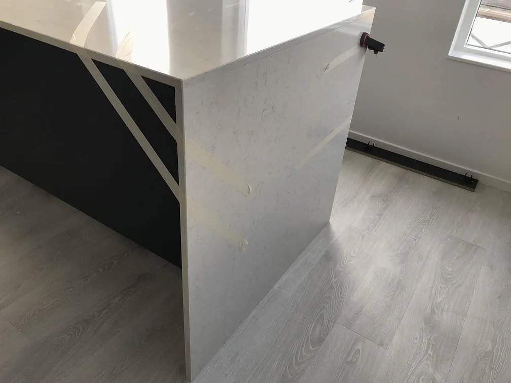 Vattenfallskant i vit Silestone Snowy Ibiza mot mörka stommar och ljust trägolv i ett kök under montering i Häljarp.