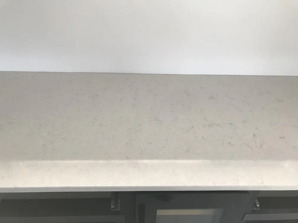 Närbild på köksö i Silestone Snowy Ibiza med vattenfallskant fastspänd mot stommen under montering i Häljarp.