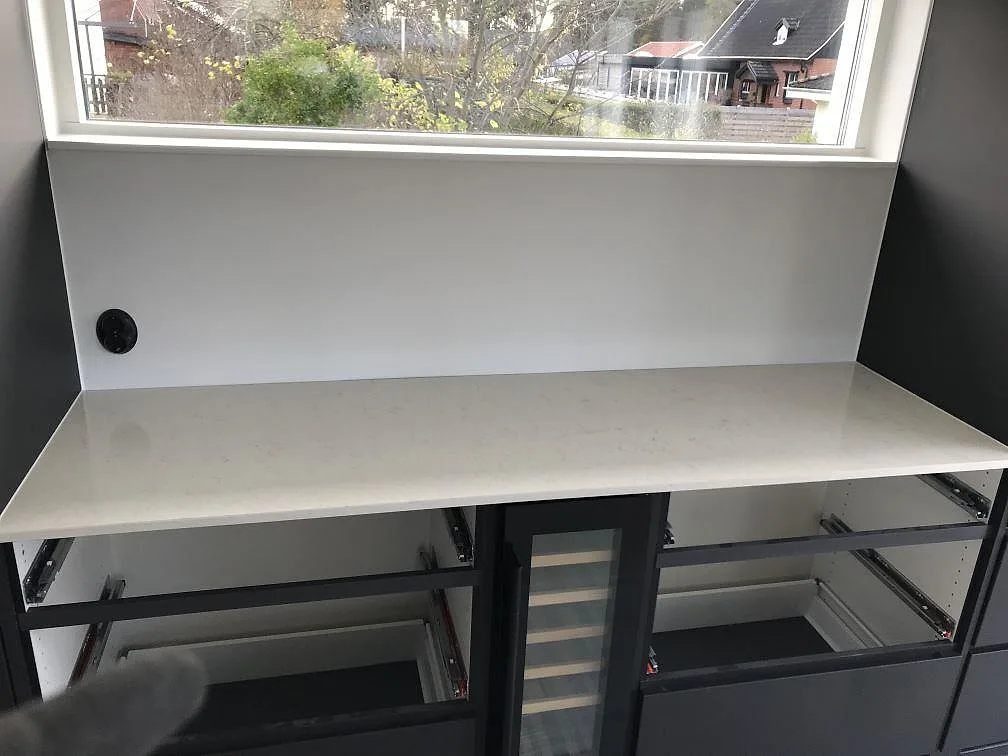 Bänkskiva i vit Silestone Snowy Ibiza under ett fönster, monterad på mörkgrå stommar i ett kök i Häljarp.