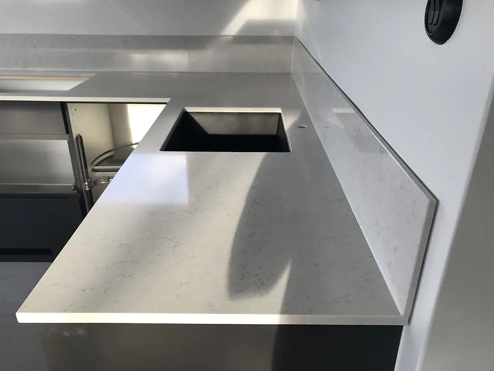 Köksbänkskiva i polerad Silestone Snowy Ibiza med underlimmad diskho och låg stänkkant i ett kök i Häljarp.