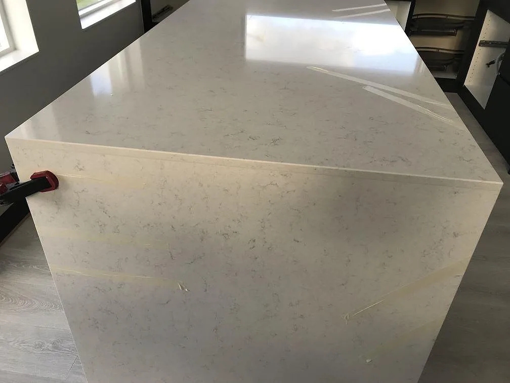 Köksö i vit Silestone Snowy Ibiza, polerad, med vattenfallskant och tejpade fogar i ett kök i Häljarp.