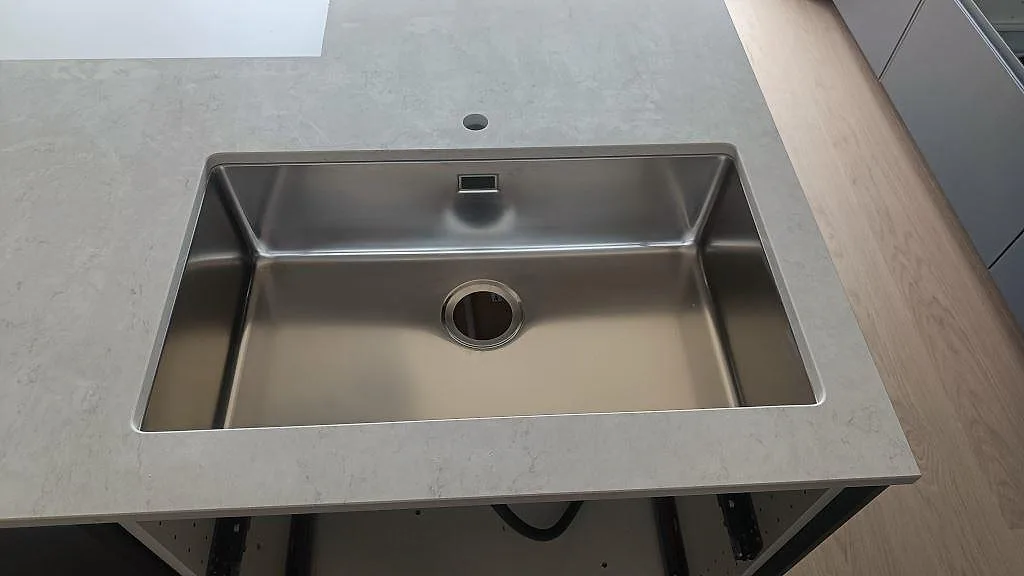 Närbild på rostfri underlimmad diskho i polerad Silestone Snowy Ibiza med ljus ådring i ett kök i Häljarp.