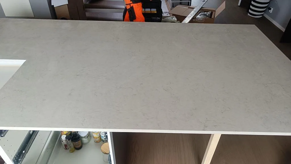 Stor bordsskiva i polerad Silestone Snowy Ibiza över öppna köksstommar under montering i Häljarp.