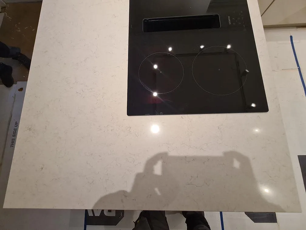 Topvy över polerad Silestone Snowy Ibiza med svart induktionshäll och ljus ådring på köksön i Hässelby.