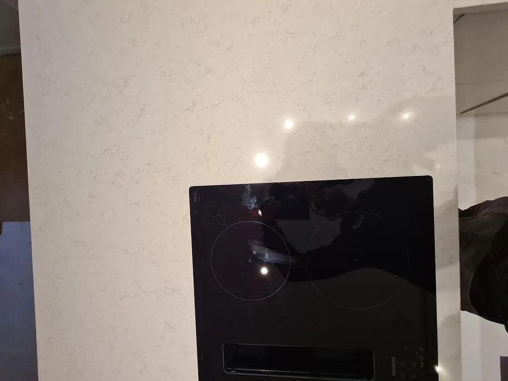 Närbild på svart induktionshäll i köksö av polerad Silestone Snowy Ibiza med diskret grå ådring i Hässelby.