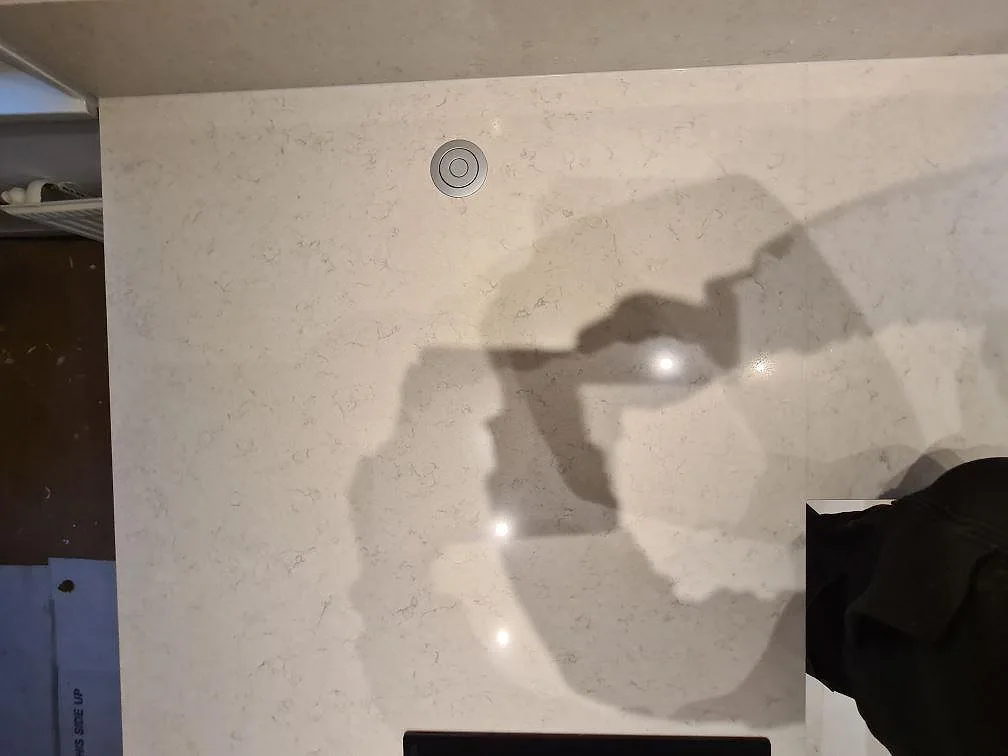 Detalj av polerad Silestone Snowy Ibiza på köksön med kabeluttag, blank yta och skuggor från montering i Hässelby.