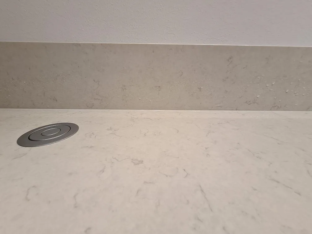 Närbild på ljus Silestone Snowy Ibiza, polerad kvartskomposit, med rund kabelgenomföring och stänkskydd i Hässelby.