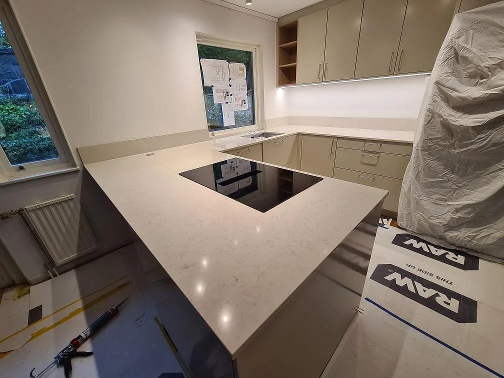 Stor köksö i polerad Silestone Snowy Ibiza, 20 mm kvartskomposit, med svart induktionshäll i ett kök under montering i Hässelby.