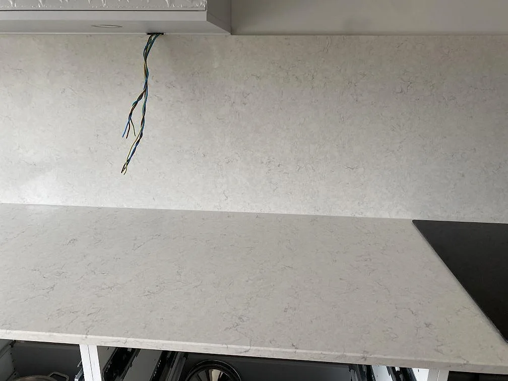 Polerad Silestone Snowy Ibiza bänkskiva och hög stänkvägg med synlig elinstallation under montering i ett kök i Halmstad.