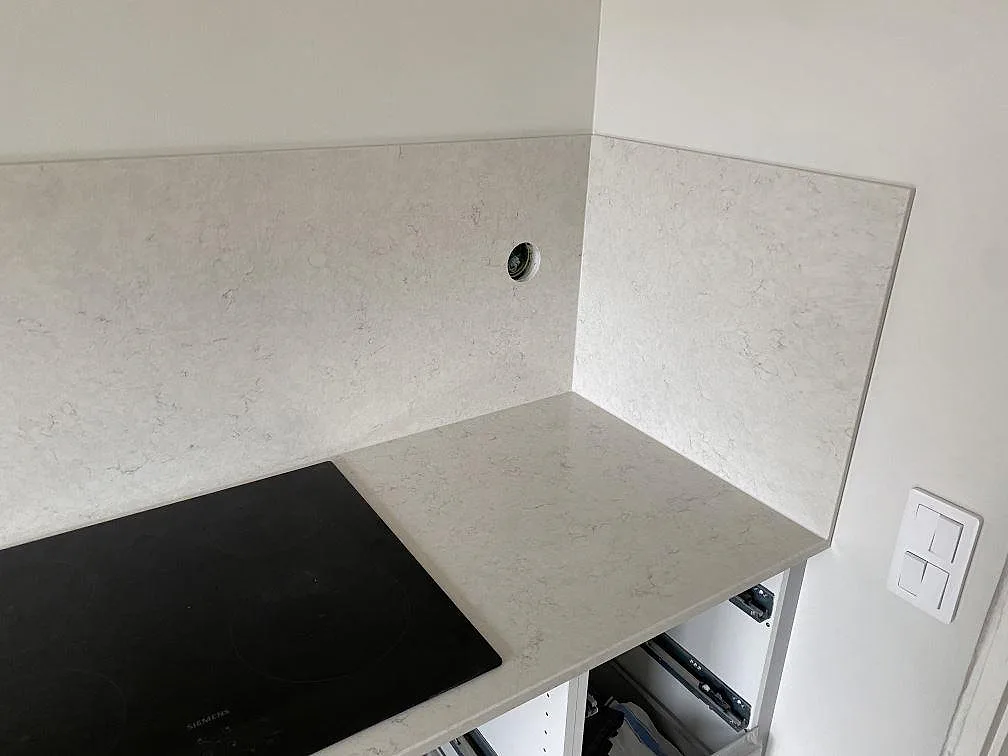 Köksbänkskiva i vit Silestone Snowy Ibiza, polerad, med infälld Siemens induktionshäll och heltäckande stänkvägg i samma sten i ett kök i Halmstad.