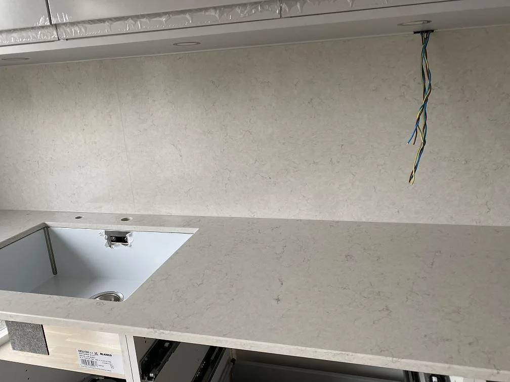 Bänkskiva och stänkvägg i Silestone Snowy Ibiza vid diskhon, fotograferad under montering med synlig elkabel, Halmstad.