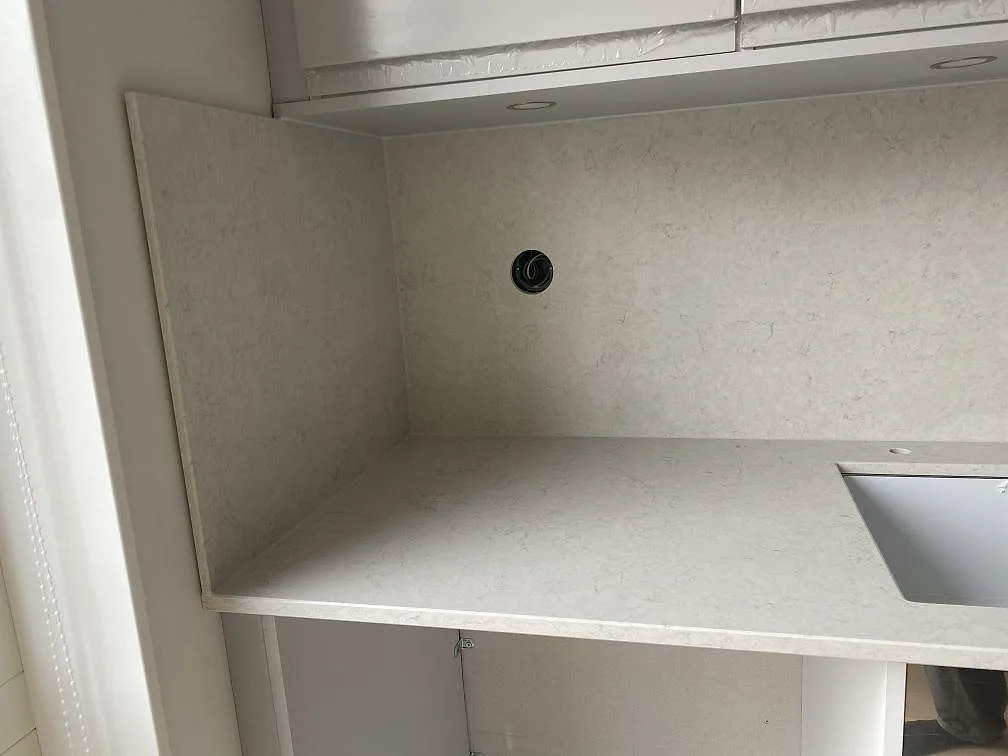 Hörnparti med heltäckande stänkväggar i Silestone Snowy Ibiza och uttag för ventilation i ett kök i Halmstad.