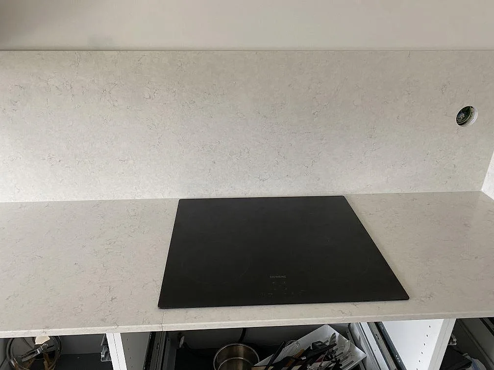 Polerad Silestone Snowy Ibiza köksbänkskiva med svart induktionshäll och uppvikt stänkparti i samma kvartskomposit, Halmstad.