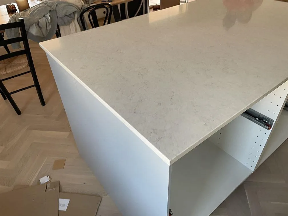 Stor köksö med polerad köksbänkskiva i vit Silestone Snowy Ibiza kvartskomposit i ett kök under montering i Halmstad.