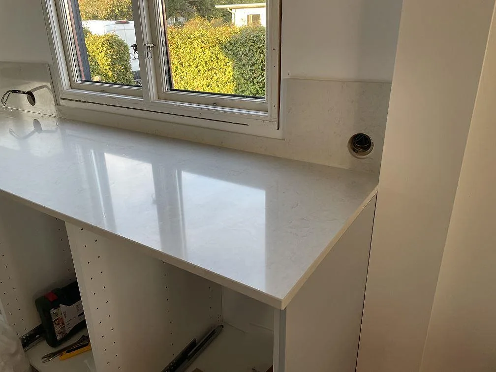Polerad Silestone Snowy Ibiza bänkskiva under stora köksfönster med trädgårdsutsikt och stänkskydd i samma sten i Halmstad.