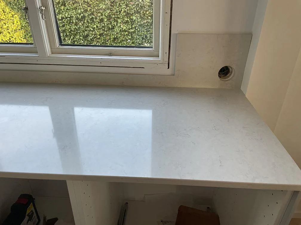 Fönstersida med polerad Silestone Snowy Ibiza bänkskiva och matchande stänkskydd ovanför öppna köksstommar i Halmstad.