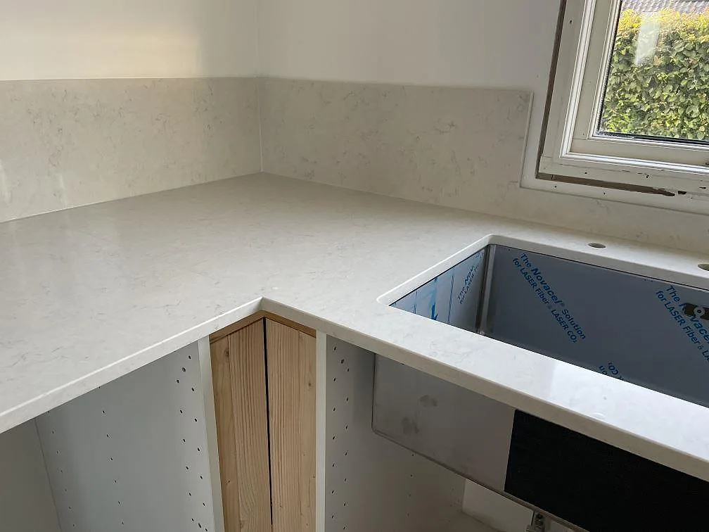 L-formad köksbänkskiva i polerad Silestone Snowy Ibiza med diskhoöppning och matchande stänkskydd i Halmstad.