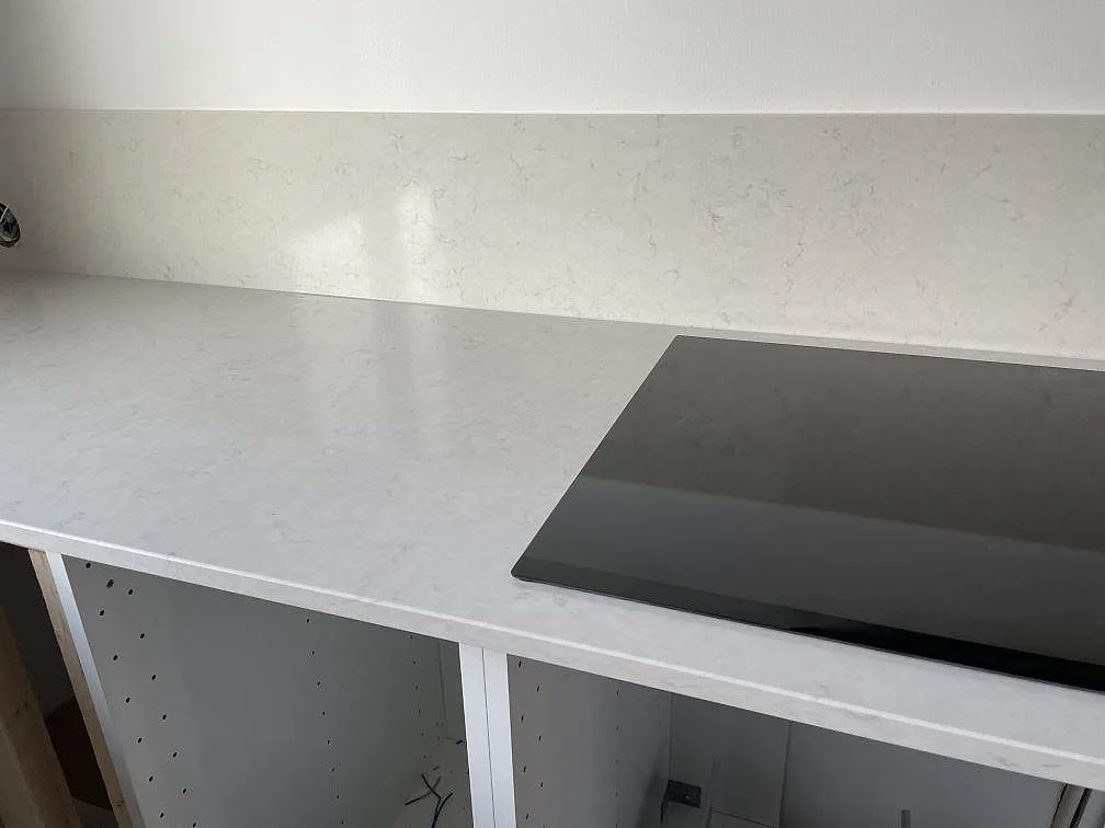Närbild på polerad Silestone Snowy Ibiza köksbänkskiva med svart induktionshäll och uppvikt stänkskydd i Halmstad.