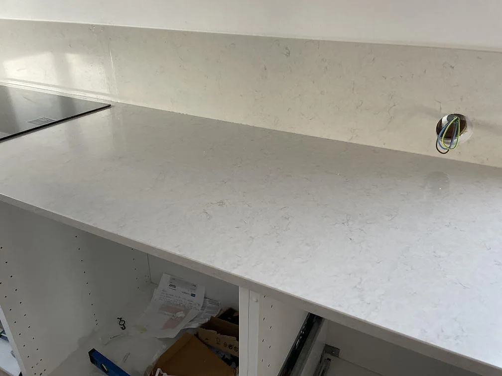 Lång väggbänk i polerad Silestone Snowy Ibiza med svart häll och elgenomföring i ett vitt kök i Halmstad.