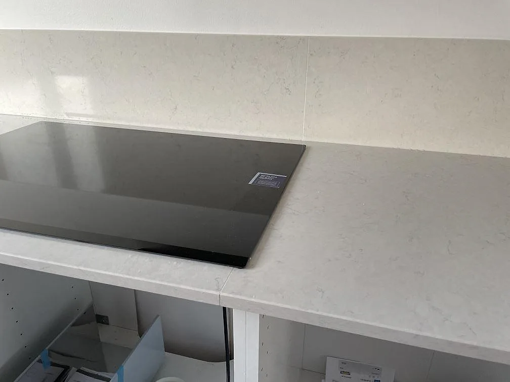 Köksbänkskiva i vit Silestone Snowy Ibiza med svart induktionshäll och polerat stänkskydd under montering i Halmstad.