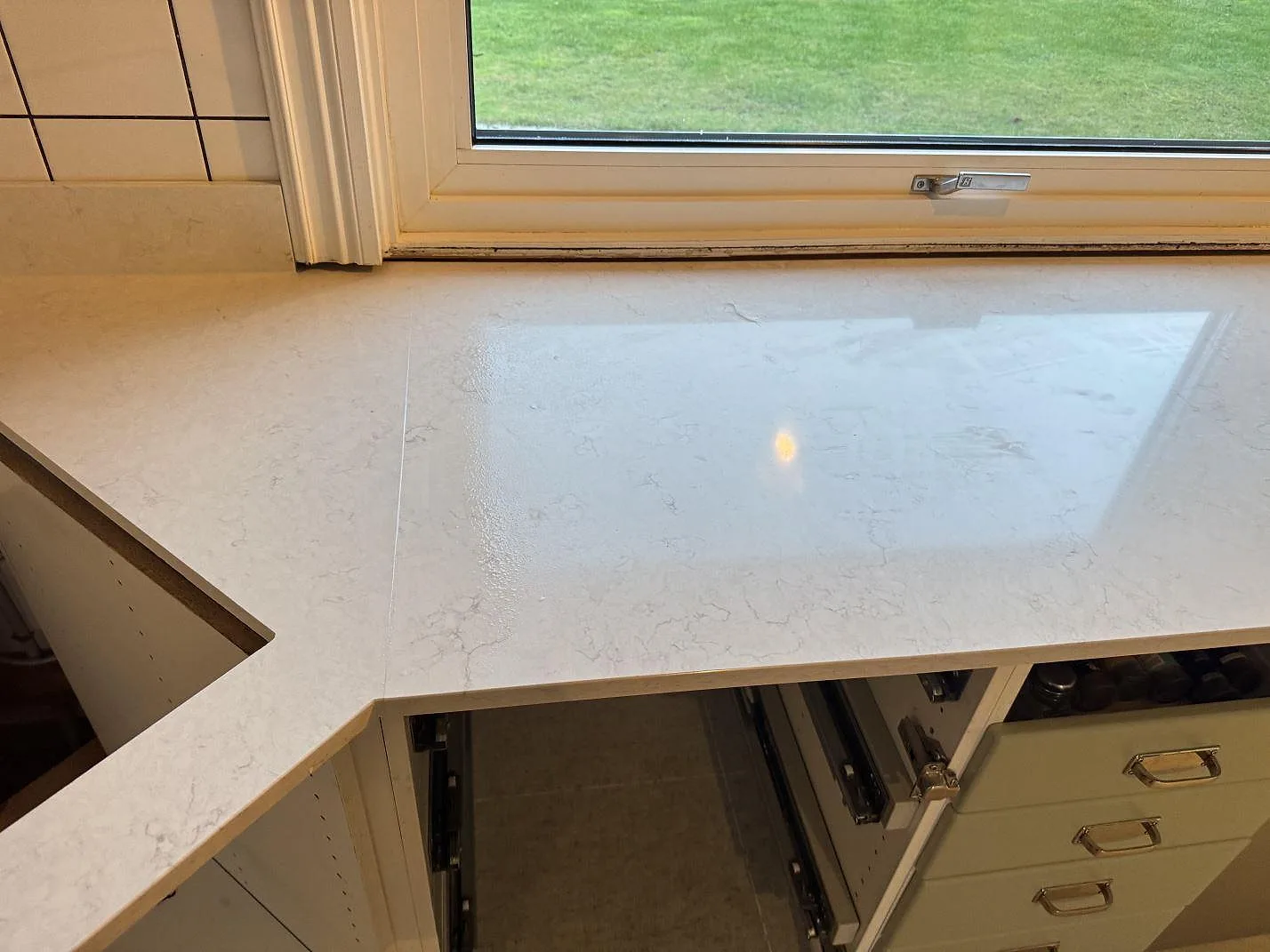 Polerad Silestone Snowy Ibiza köksbänk längs fönstret med synlig ljusgrå ådring och spegelblank yta i ett kök i Halmstad.