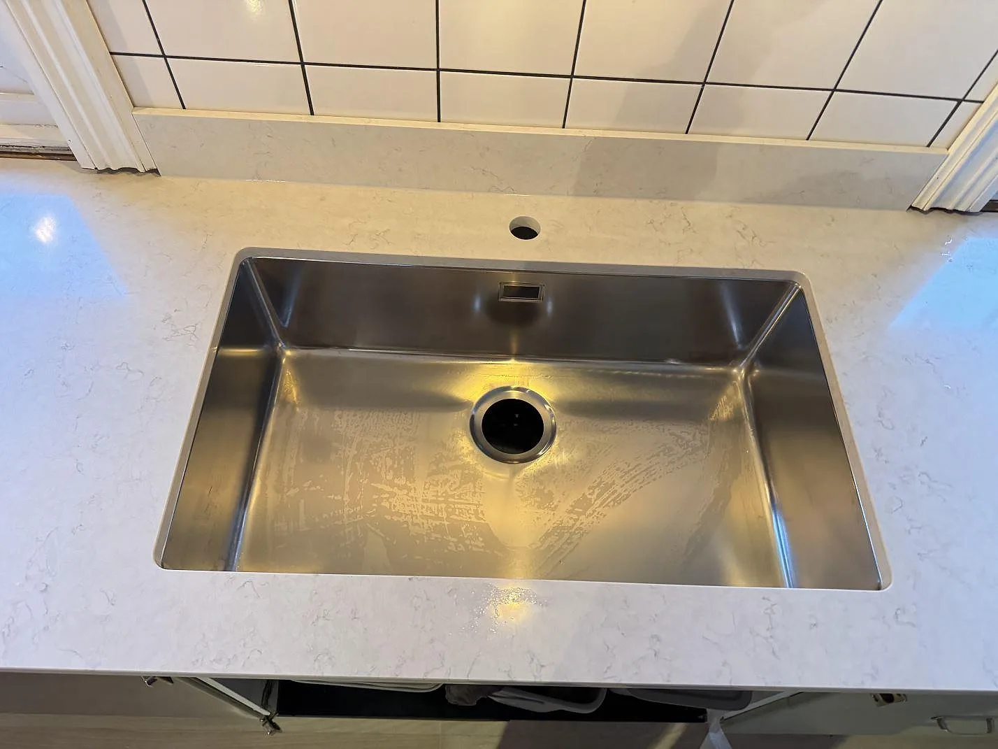 Närbild ovanifrån på den underlimmade rostfria diskhon i en polerad Silestone Snowy Ibiza bänkskiva i ett kök i Halmstad.
