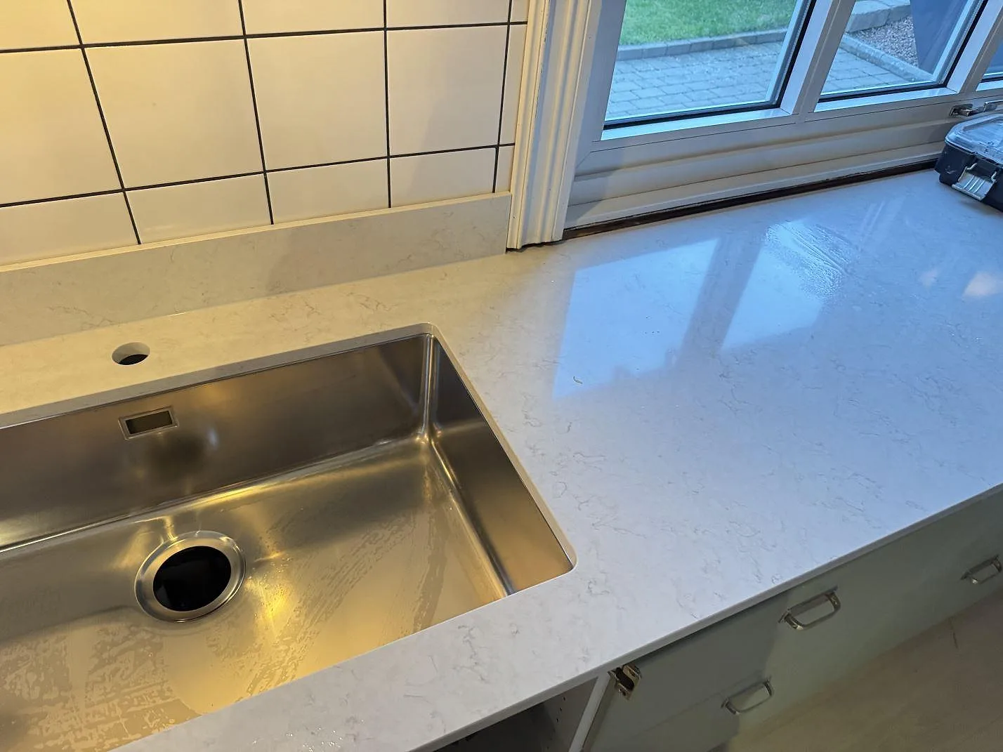 Diskhörnan med underlimmad rostfri ho och polerad Silestone Snowy Ibiza bänkskiva mot vit kakel och fönster i Halmstad.