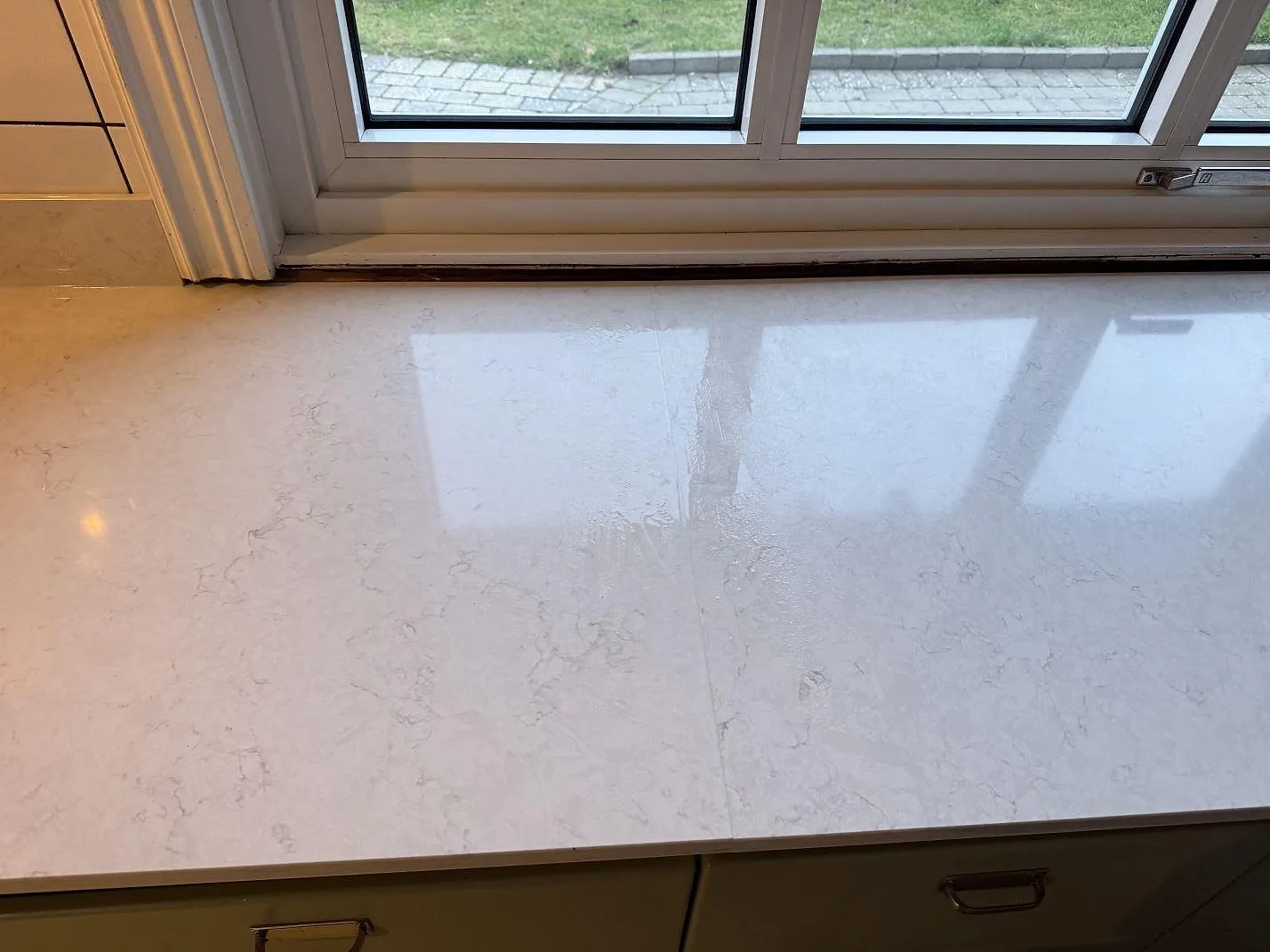 Ovanifrån på den polerade Silestone Snowy Ibiza bänkskivan med fönsterspegling som visar den fina ådringen i ett kök i Halmstad.