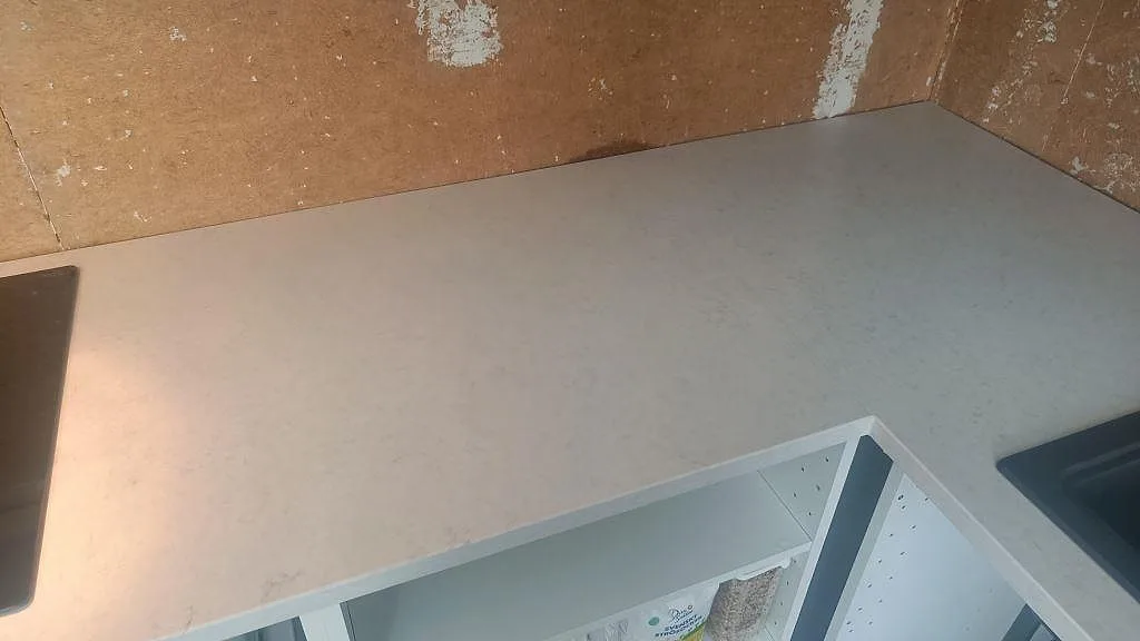 Hörndel av köksbänkskiva i Silestone Snowy Ibiza, Mocka, med ljus ådring och svart diskho i Harestad.