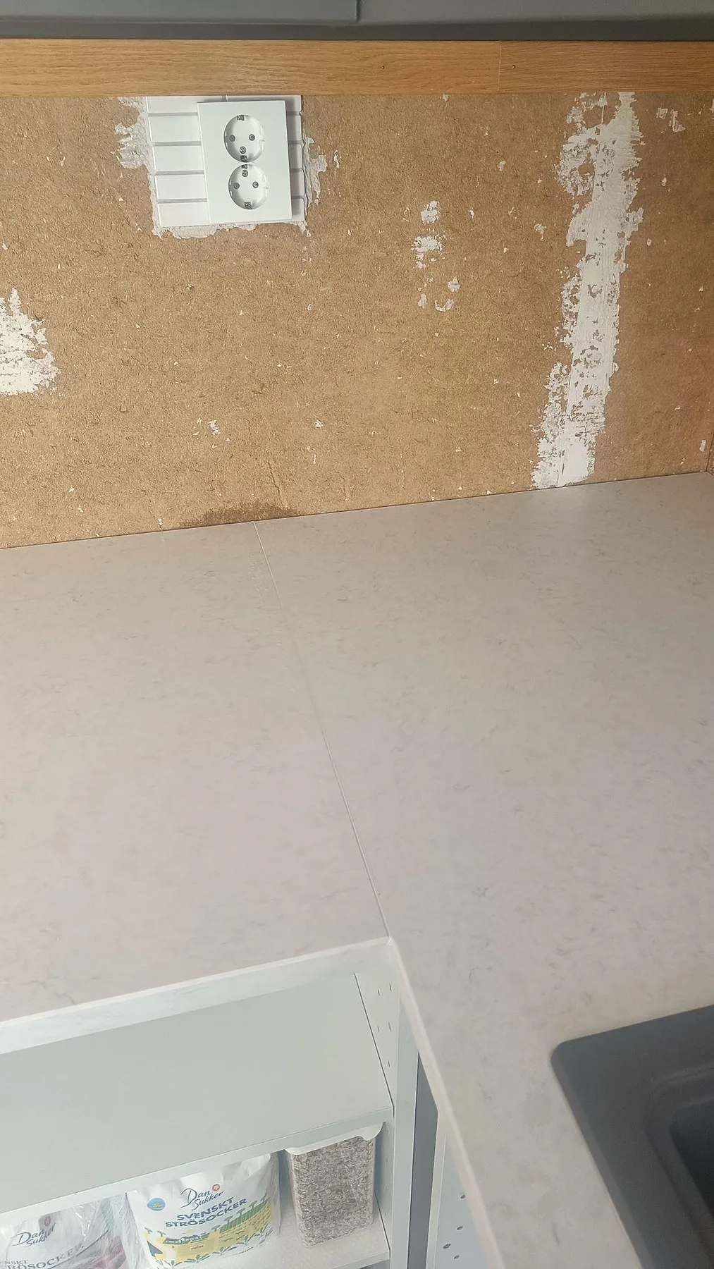 Detalj av L-formad Silestone Snowy Ibiza-bänkskiva, Mocka, vid vägguttag och svart diskho i Harestad.