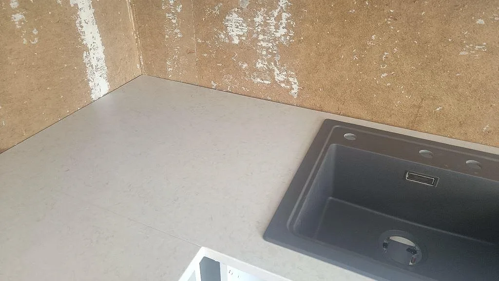 Underlimmad svart diskho i bänkskiva av Silestone Snowy Ibiza, Mocka, med oskodd vägg under köksmontering i Harestad.