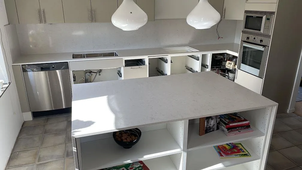 Polerad köksbänkskiva i kompositstenen Silestone Snowy Ibiza med köksö, stänkskydd och rostfri diskho i ett kök i Helsingborg.