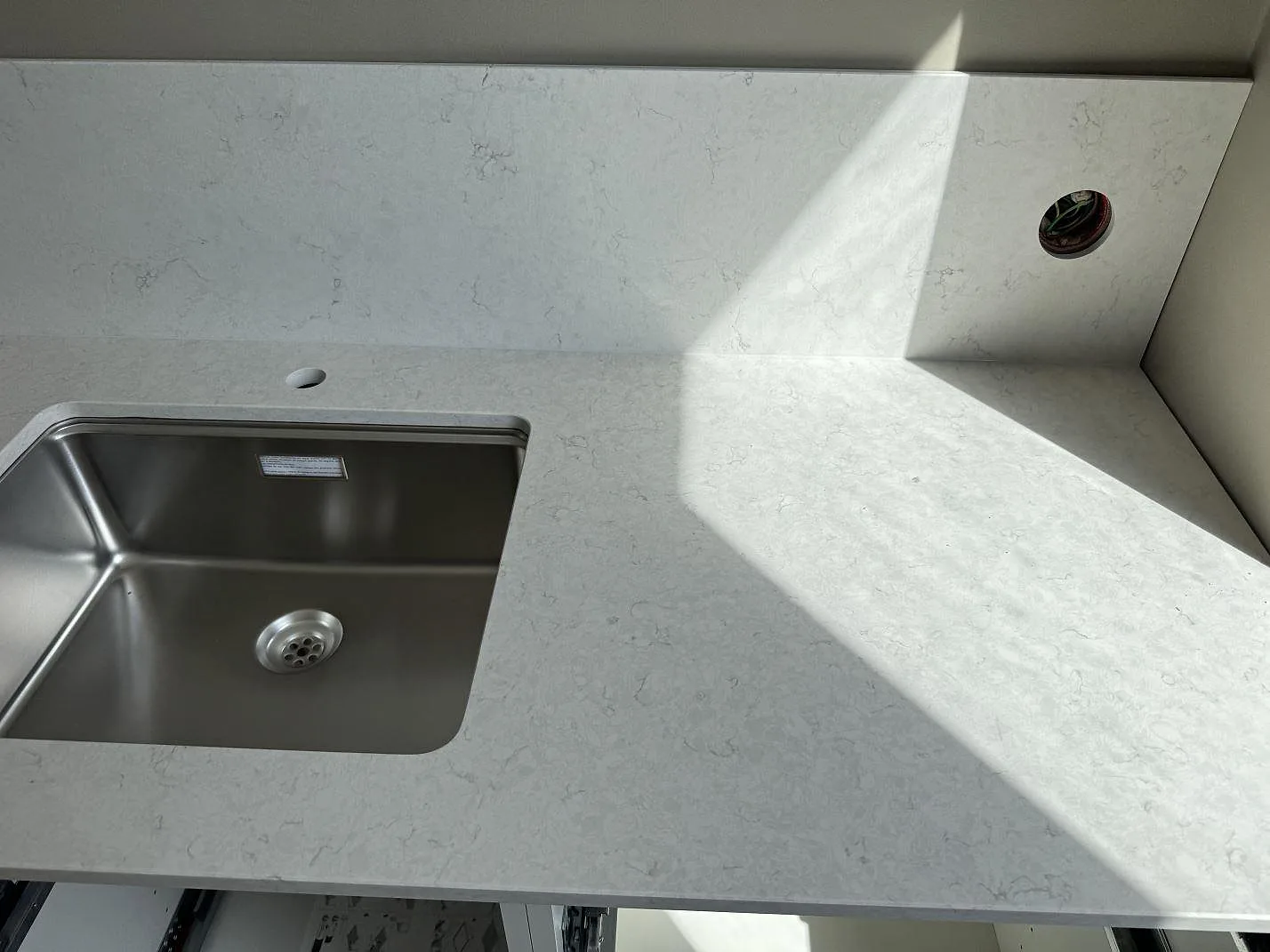 Närbild av vit kompositbänkskiva i Silestone Snowy Ibiza Mocka med rostfri diskho, stänkskydd och fönsternisch i Helsingborg.