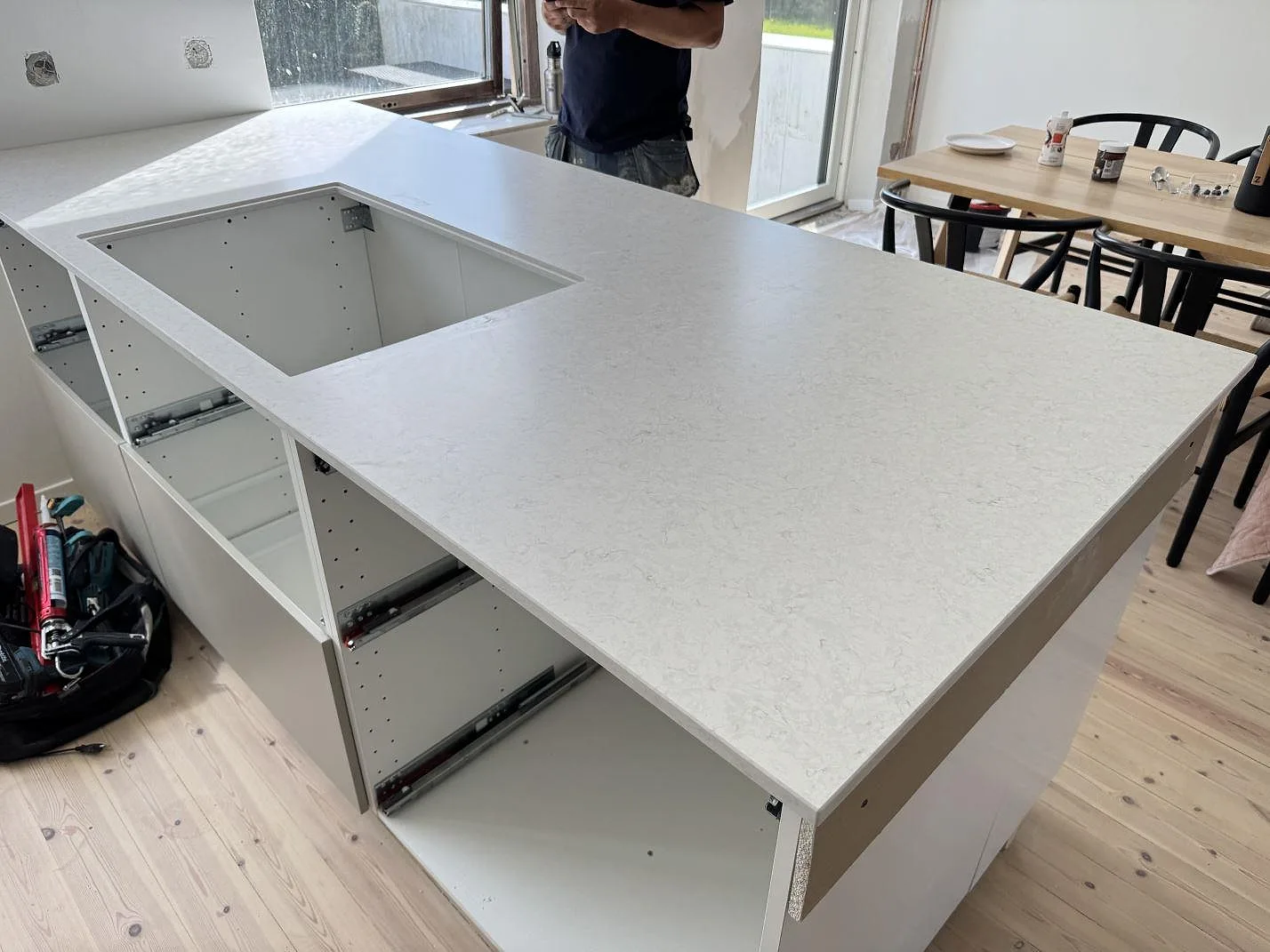 L-formad köksbänkskiva i matt Silestone Snowy Ibiza Mocka med hällöppning och öppna köksstommar under montering i Helsingborg.