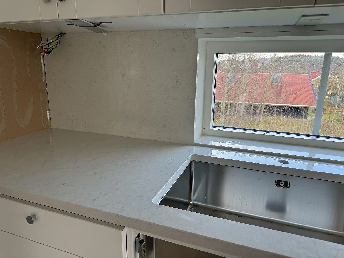 Polerad Silestone Snowy Ibiza som köksbänkskiva i komposit med rostfri diskho under stenen och stort fönster i Hisings Kärra.