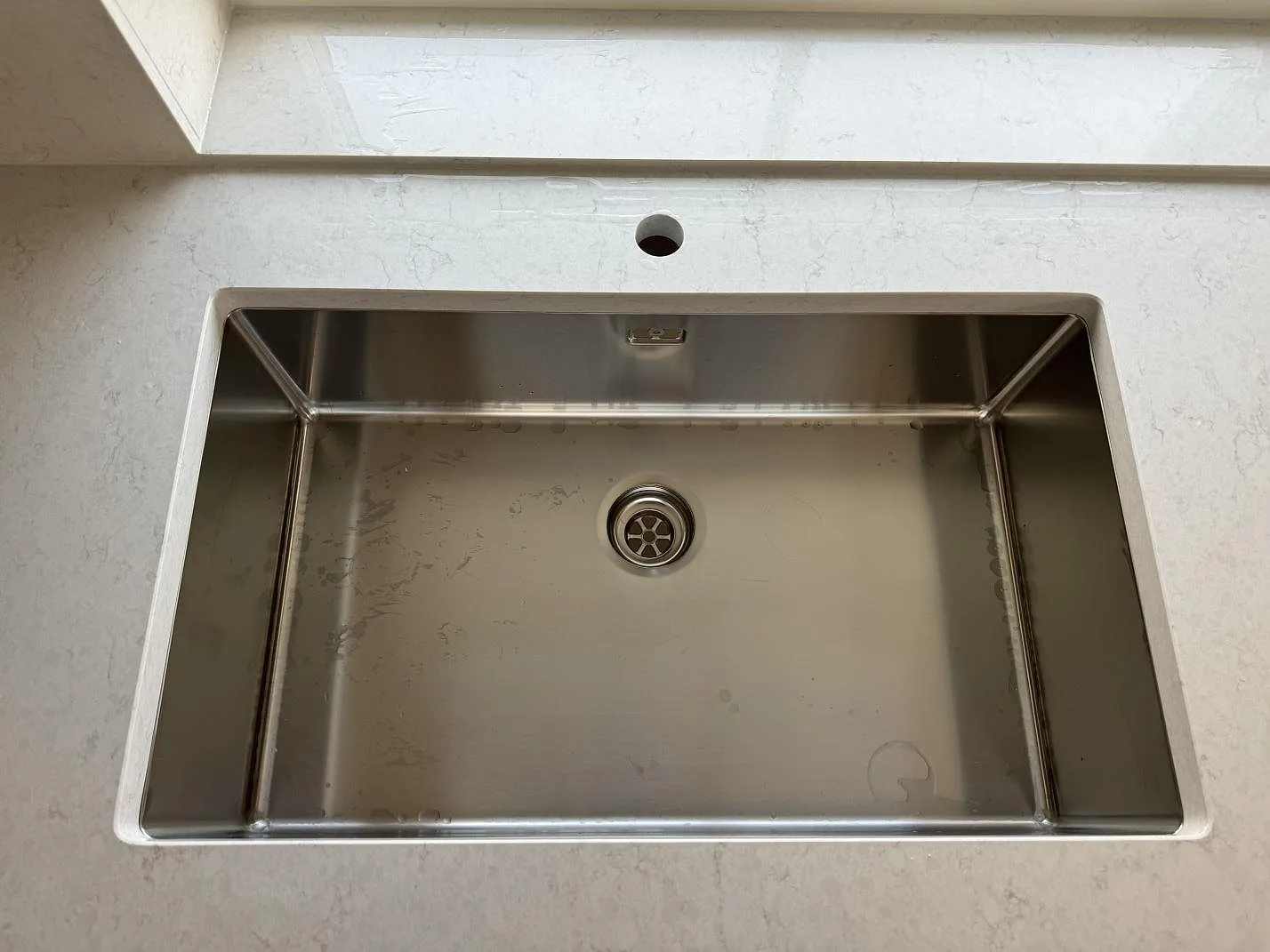 Närbild på underlimmad rostfri diskho i en polerad Silestone Snowy Ibiza köksbänkskiva med blandarhål i Hisings Kärra.