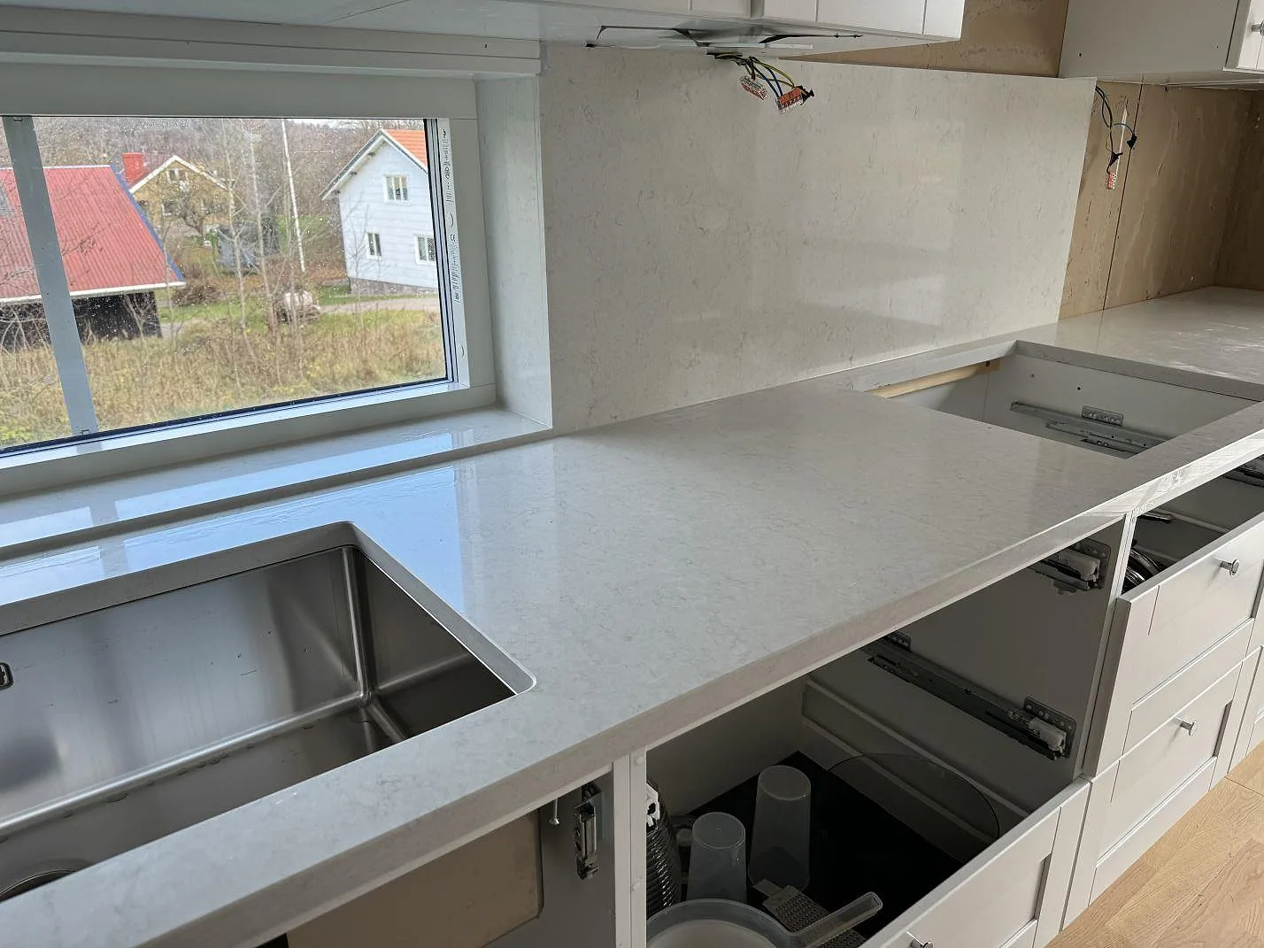 L-formad köksbänkskiva i polerad Silestone Snowy Ibiza, komposit, med underlimmad rostfri diskho och hällöppning i ett kök i Hisings Kärra.