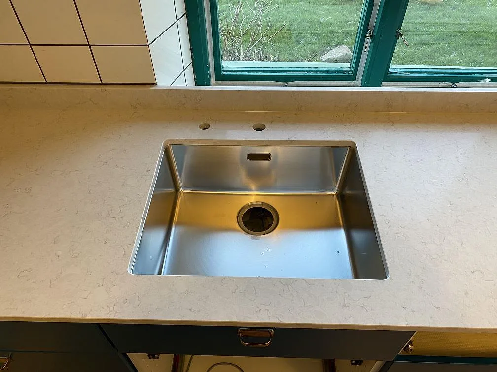 Rostfri diskho i en polerad köksbänkskiva av Silestone Snowy Ibiza, ljus kvartskomposit med låg stenkant vid fönster i Höganäs.