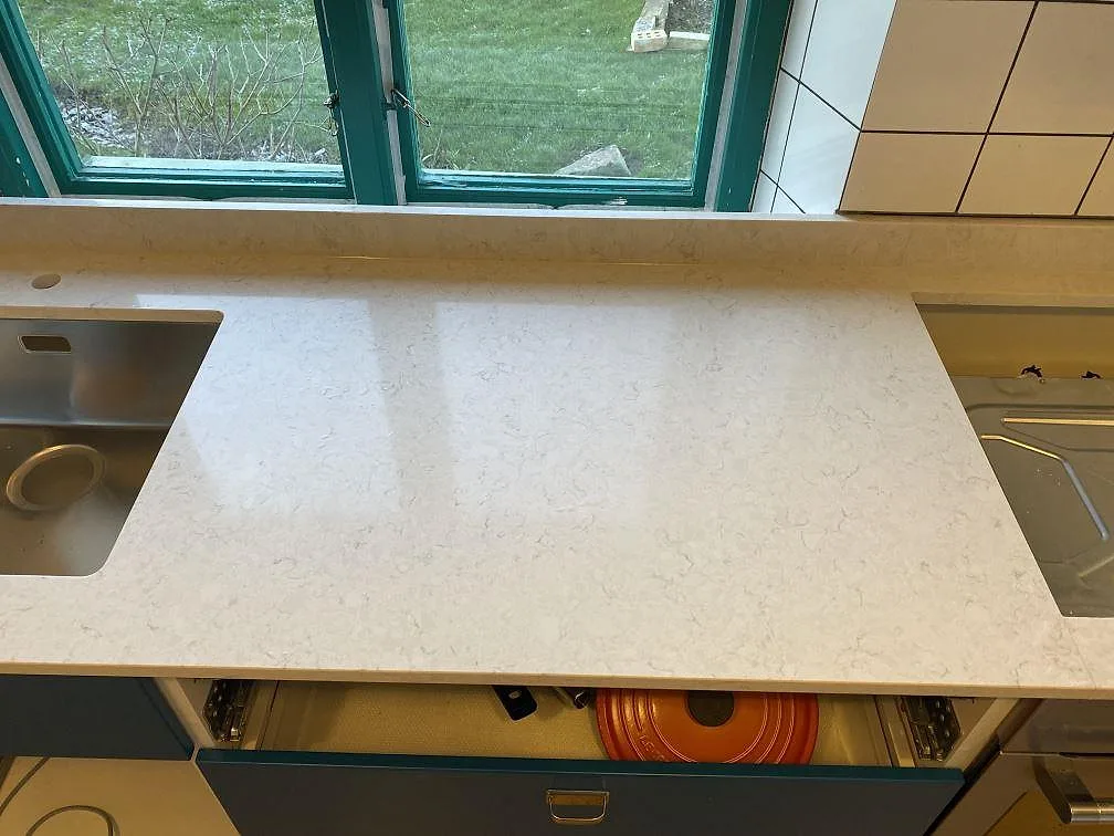 Arbetsyta i polerad Silestone Snowy Ibiza mellan rostfri ho och öppning för spis, ljus kompositbänkskiva i ett kök i Höganäs.