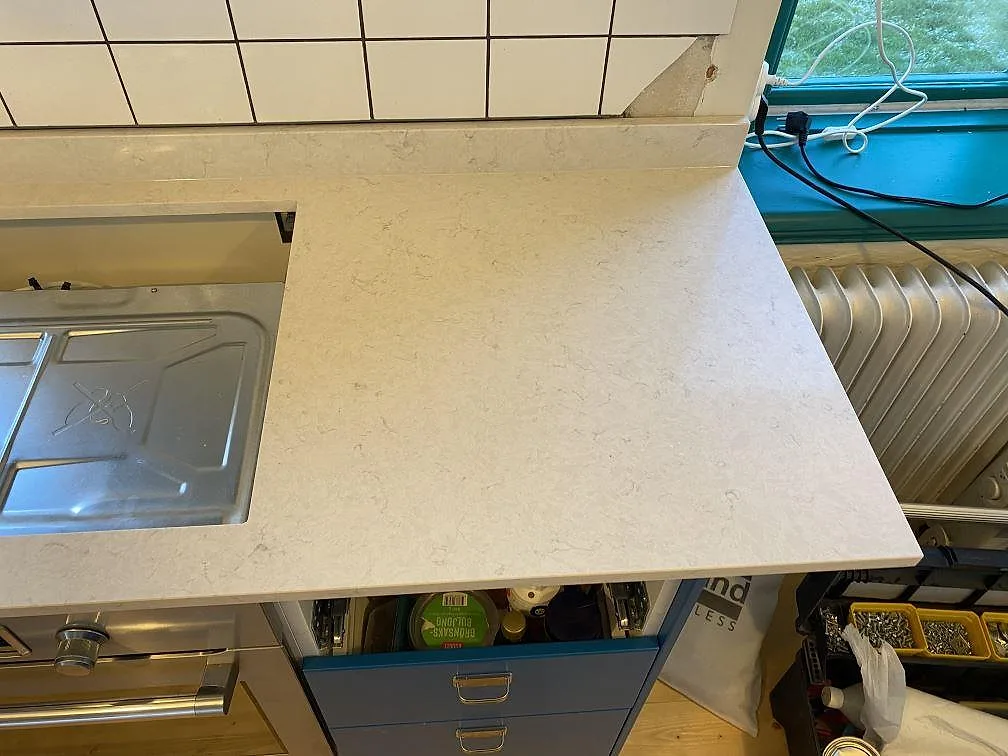 Höger del av köksbänkskiva i polerad Silestone Snowy Ibiza, ljus kvartskomposit vid fönster och radiator i Höganäs.