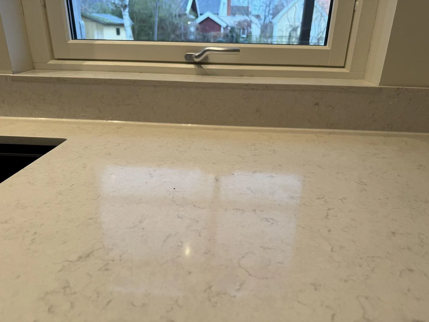Närbild på den polerade ytan i Silestone Snowy Ibiza med diskret grå ådring vid fönstret i Höllviken.