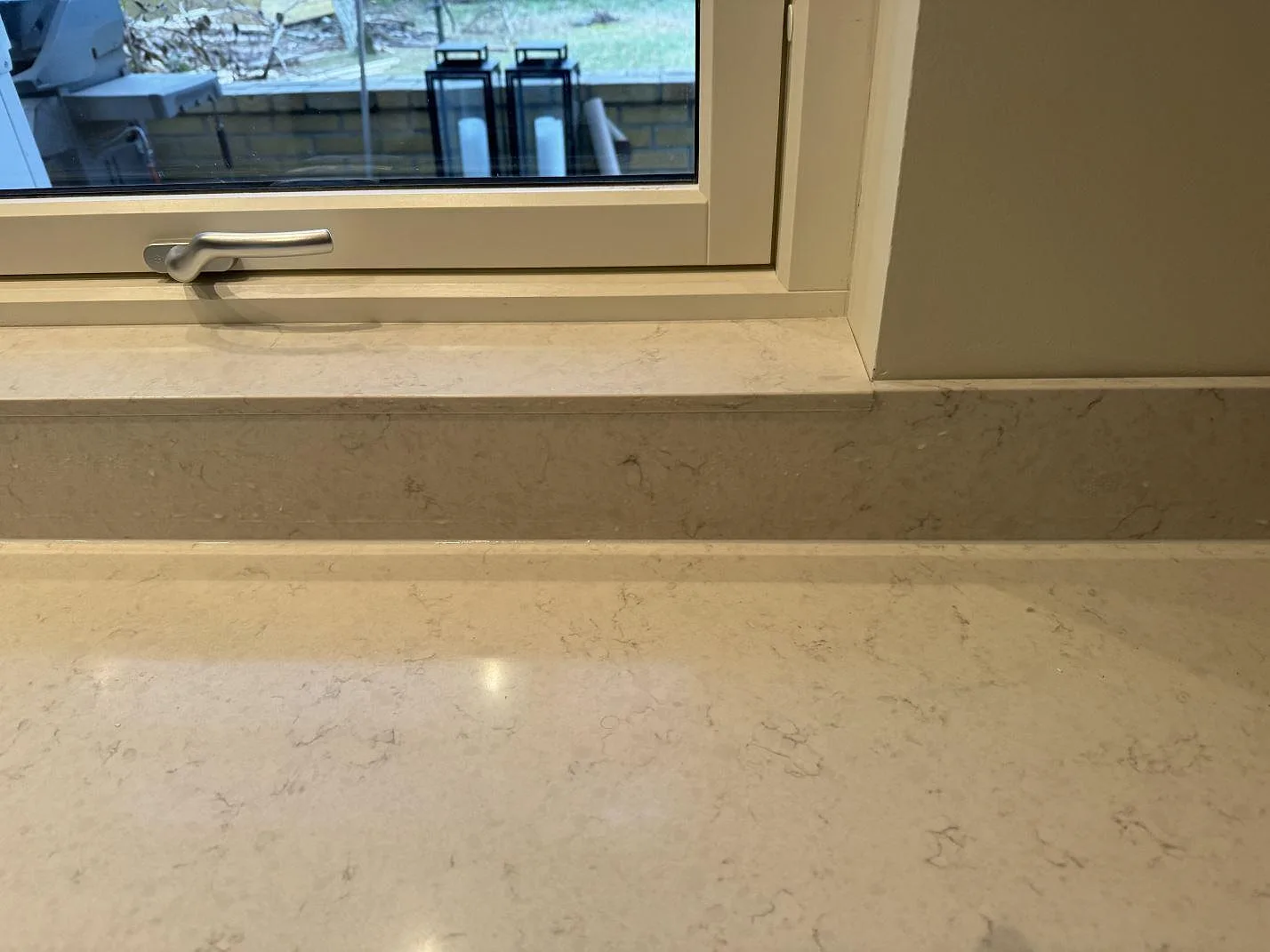 Stänkskydd och fönsterbänk i polerad Silestone Snowy Ibiza ovanför den ljusa köksbänken i Höllviken.