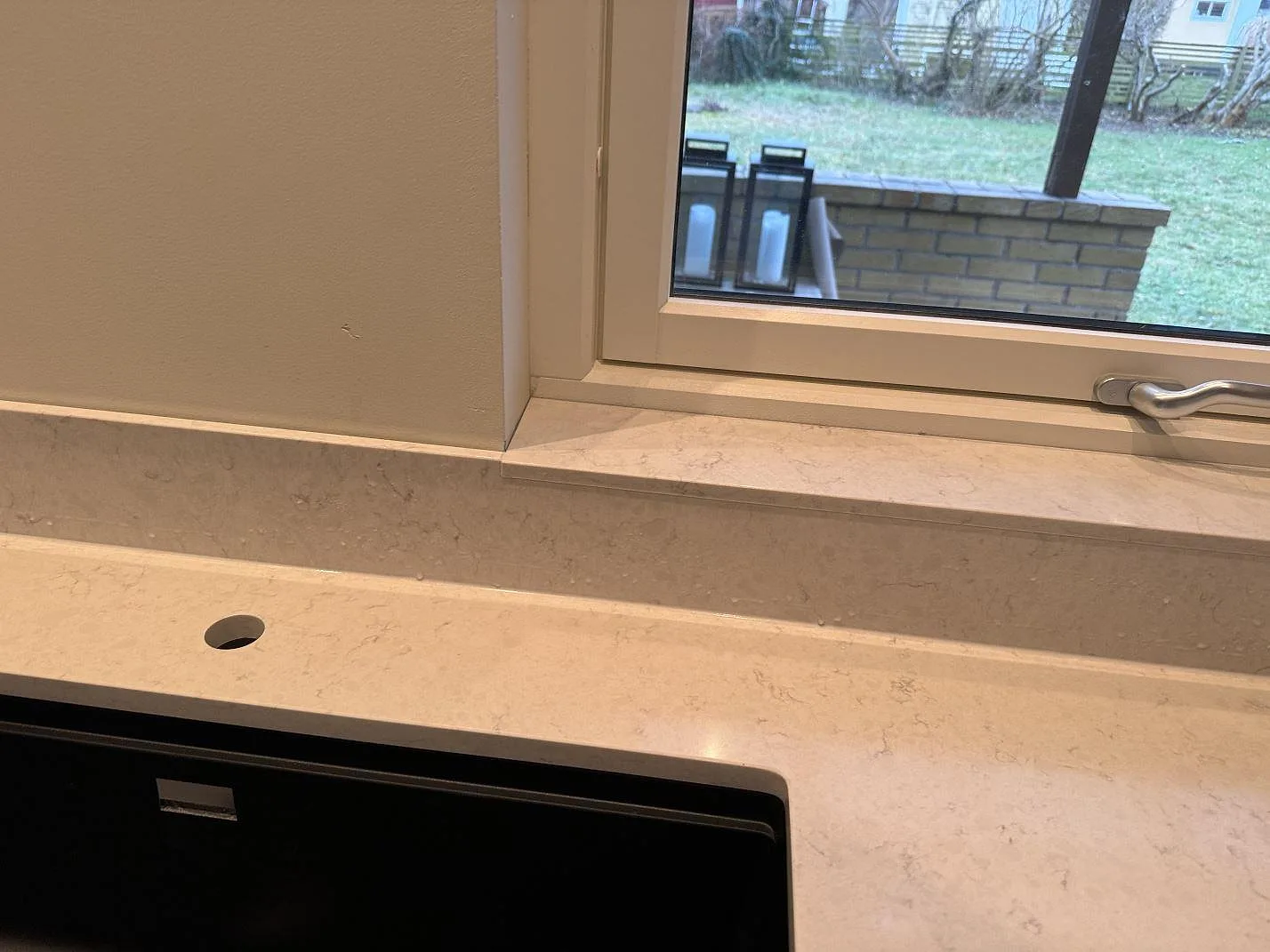 Detalj av svart diskho monterad under polerad Silestone Snowy Ibiza med blandarhål framför fönstret i Höllviken.