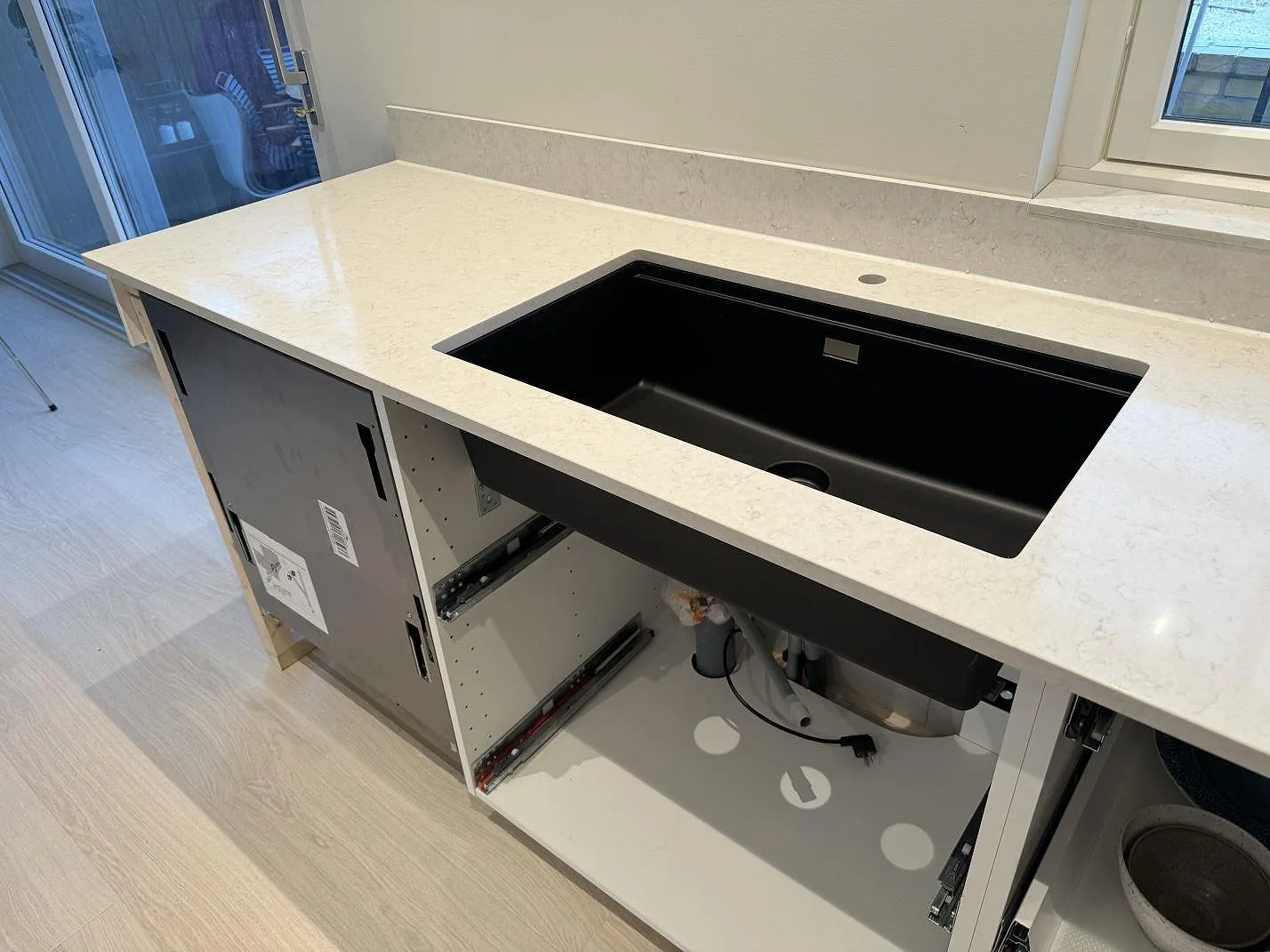 Ljus köksbänkskiva i polerad Silestone Snowy Ibiza med svart diskho och fönsternära stänkskydd i ett kök i Höllviken.