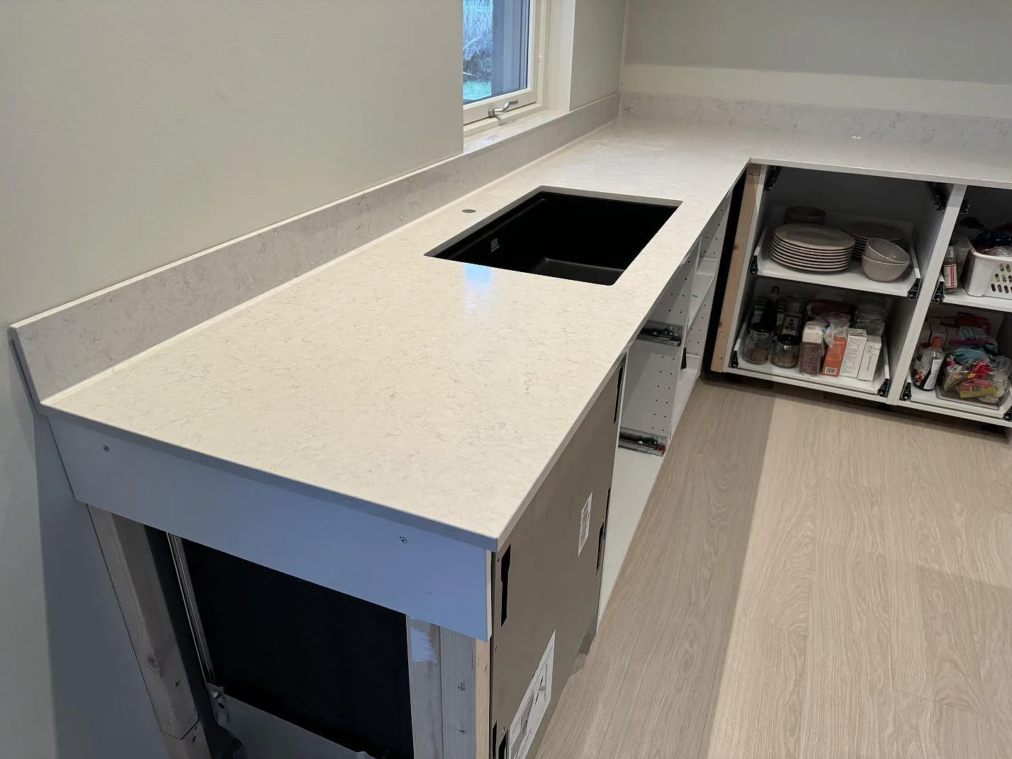 Polerad köksbänkskiva i Silestone Snowy Ibiza med svart underlimmad diskho, stänkskydd och öppna köksstommar i Höllviken.