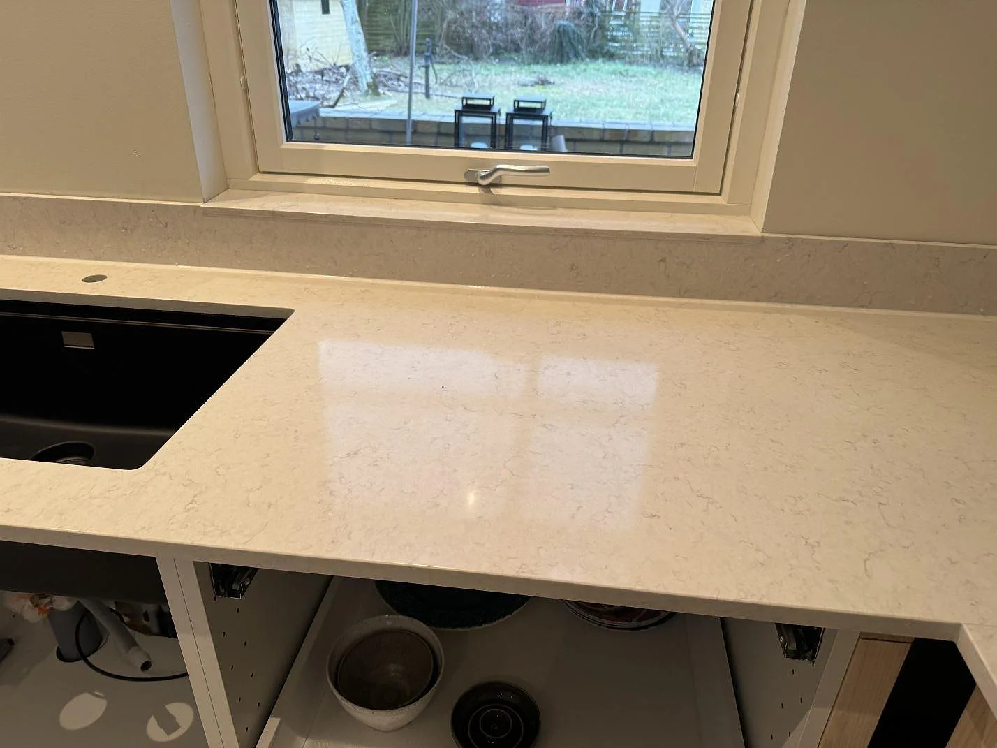 Polerad Silestone Snowy Ibiza som bänkskiva under fönster med svart diskho och matchande stänkskydd i Höllviken.