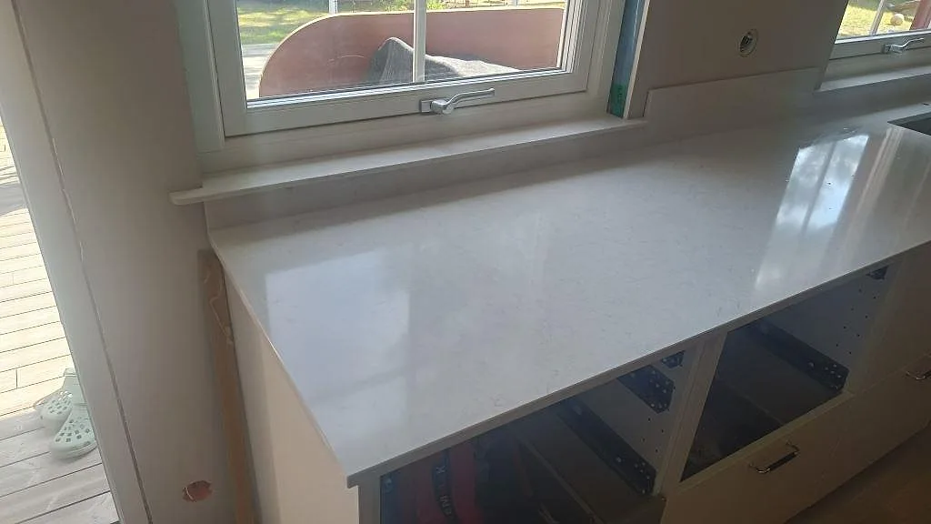 Polerad Silestone Snowy Ibiza längs fönsterväggen med låg stänkkant och öppna stommar under montering i Höllviken.