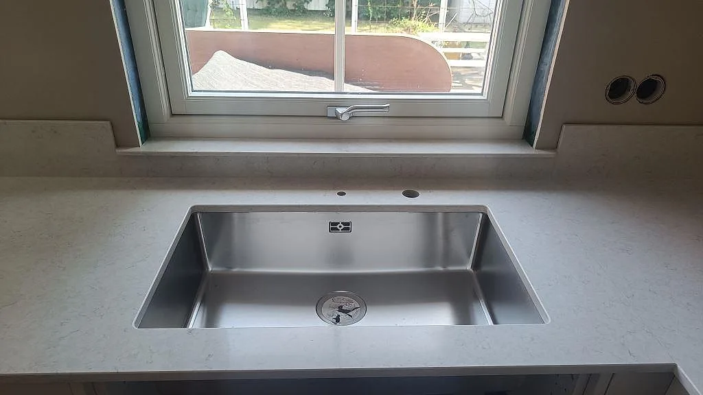Underlimmad rostfri diskho i polerad Silestone Snowy Ibiza med låg stänkkant och fönster ovanför i Höllviken.